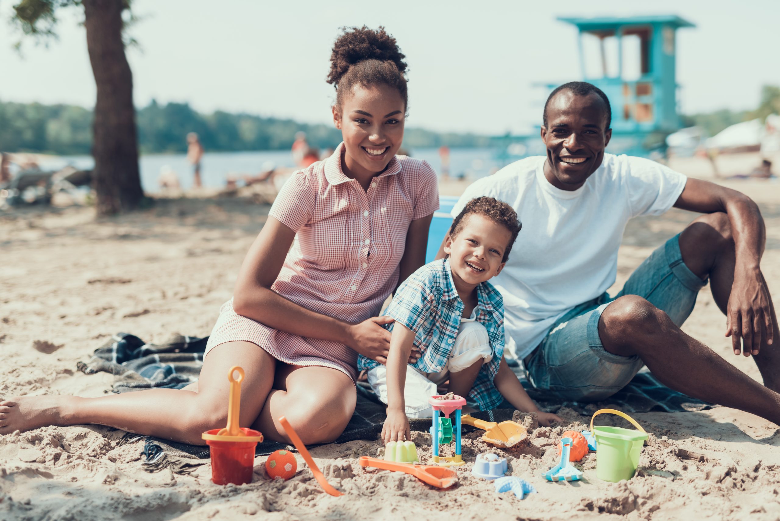Young Afro-American Family is Sitting on Sandy River Beach.